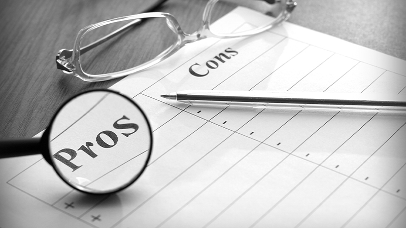 Black and white image of a blank paper with Pros and Cons label, a pen and a pair of glasses